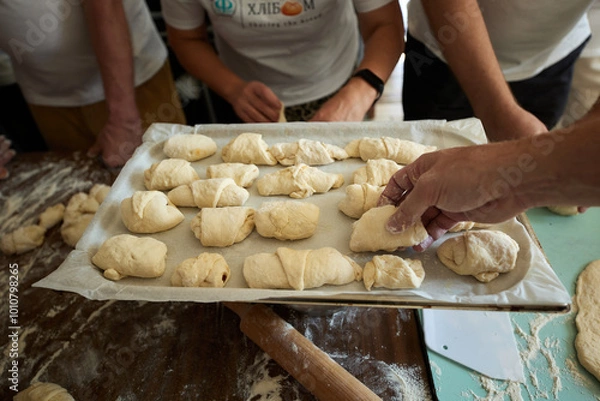Obraz A group of people stand around a wooden table and make buns from dough and jam.