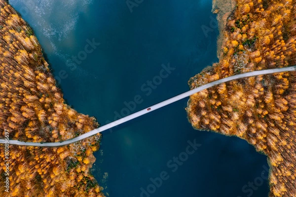 Fototapeta Aerial view of bridge road with red car over blue water lake or sea with island and autumn color woods in Finland.