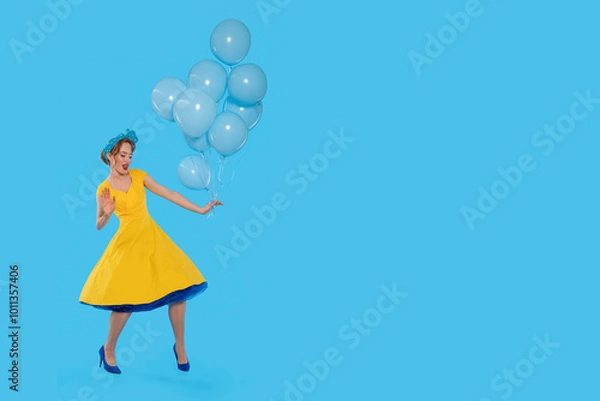 Fototapeta A joyful celebration of color as a woman in a vibrant yellow dress dances with blue balloons against a bright backdrop