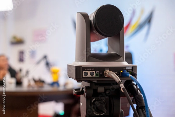 Fototapeta PTZ camera connected with HDMI, 3G-SDI, NDI, and DC12V cables, capturing a livestreaming podcast video in a content creator studio with a blurred background for depth.