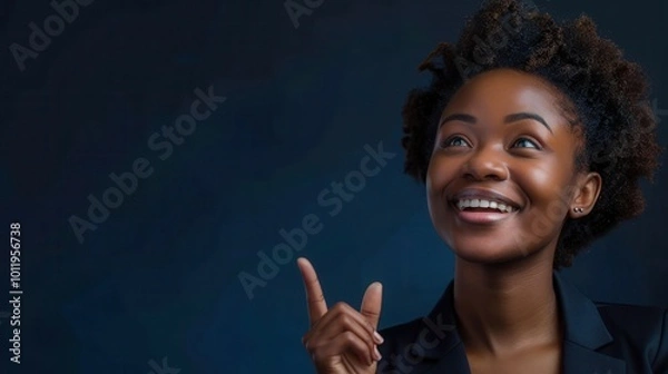 Fototapeta Optimistic Black Woman Smiling and Pointing Upwards on Dark Background