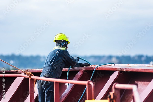 Fototapeta A deck crew member prepares the forward mooring station for docking, focused on securing the ship safely as it approaches the port. The intensity of the task contrasts with the calm surroundings.