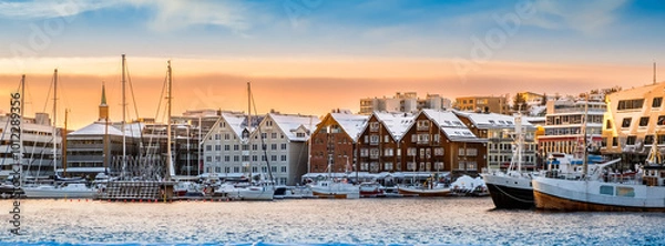 Fototapeta Tromso harbor at sunset in winter, Norway. View of Scandinavian buildings and boats in port of Tromso. Snowy winter landscape in arctic circle town in far northern Norway
