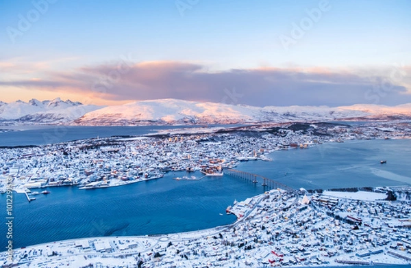 Fototapeta Aerial view of Tromso, Norway at sunset in winter from Storsteinen mountain. Tromsoya island with snowy roofs of Tromso downtown, harbor, Sandnessundet Bridge over Fjord and mountains in background