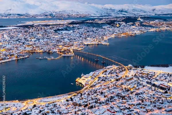 Fototapeta Aerial view of Tromso, Norway with city lights in winter from Storsteinen mountain. Tromsoya island with snowy roofs of Tromso town, harbor, Sandnessundet bridge over Fjord and mountains