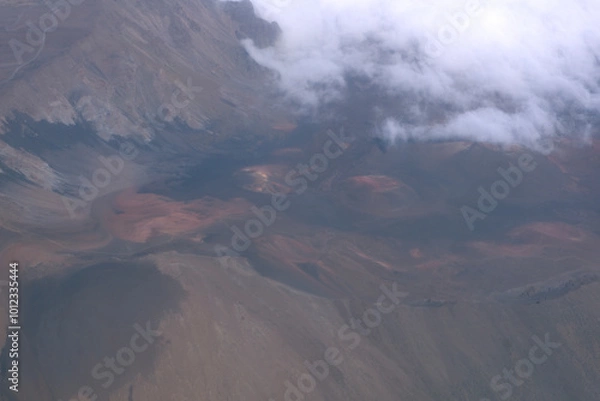 Fototapeta Aerial view of rugged mountain terrain with clouds and rocky landscapes during a cloudy day
