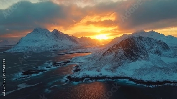 Fototapeta A scenic aerial view of snow-capped mountains and a body of water, with the sun setting behind the mountains, casting a warm glow on the landscape.