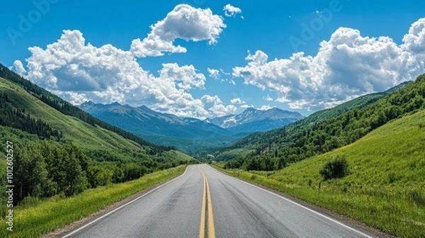 Fototapeta An asphalt road weaving through green mountain scenery, with a sunny sky and fluffy white clouds on a clear day.