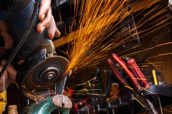 Fototapeta Worker cutting metal with grinder. Sparks while grinding iron. S