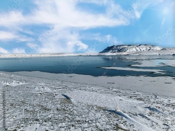 Fototapeta Lake in the winter with snow on the ground and a mesa in the background 