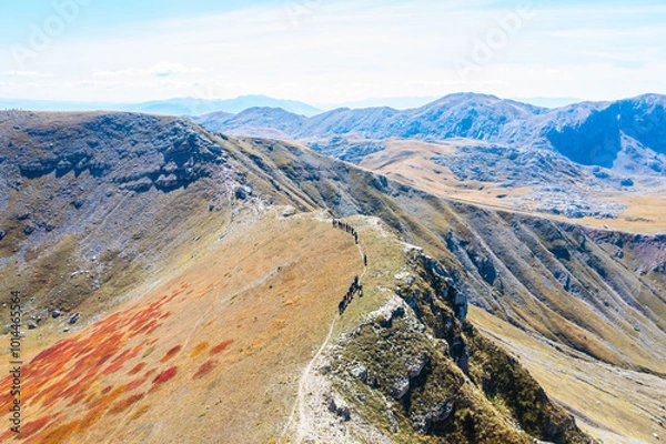 Fototapeta Hikers one behind the other in a hiking line on the ridge of a beautiful mountain during autumn with colorful vegetation - drone aerial shot