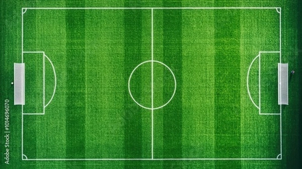 Fototapeta Aerial view of a green soccer field with white lines, empty except for a few players training in the distance, captured from directly overhead by a drone