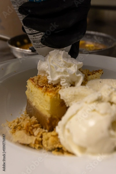 Fototapeta Cheese cake, bananas, caramel dessert. Making dessert behind the scenes. Vanilla Ice cream, whip cream topped on cheese cake, banana sauce topping with caramel on top. 