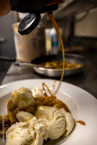 Fototapeta Cheese cake, bananas, caramel dessert. Making dessert behind the scenes. Vanilla Ice cream, whip cream topped on cheese cake, banana sauce topping with caramel on top. 