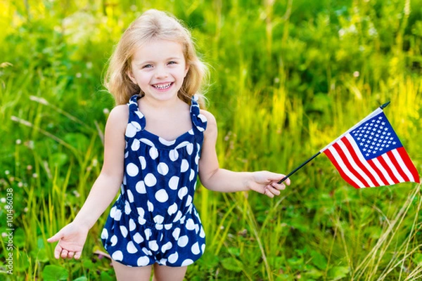 Obraz Smiling little girl with long curly blond hair holding american flag and waving it, outdoor portrait on sunny day in summer park. Independence Day, Flag Day concept