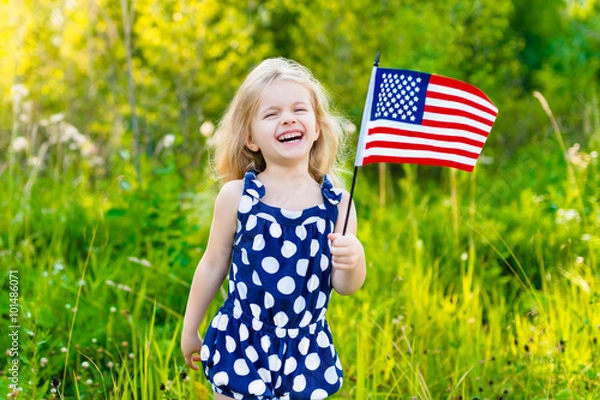 Obraz Adorable laughing little girl with long curly blond hair holding american flag and waving it on sunny day in summer park. Independence Day, Flag Day concept