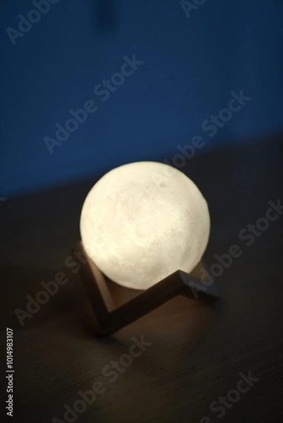 Fototapeta Hands holding an illuminated moon-like sphere lamp against a dark backdrop