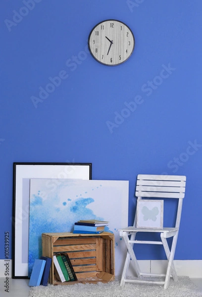 Fototapeta Room design with white chair, bookcase, pictures and clock over blue wall