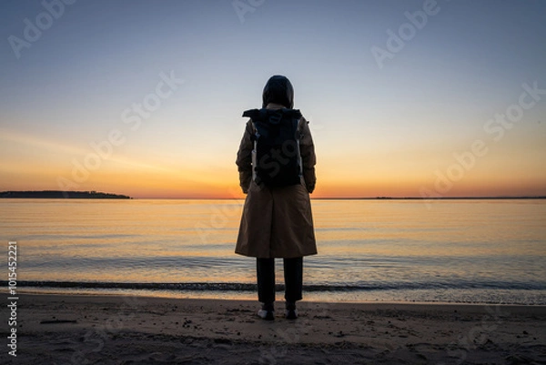 Obraz A girl in a coat with a backpack on the seashore at sunset