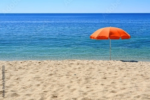 Fototapeta Serene beach scene with single orange umbrella clear blue sky