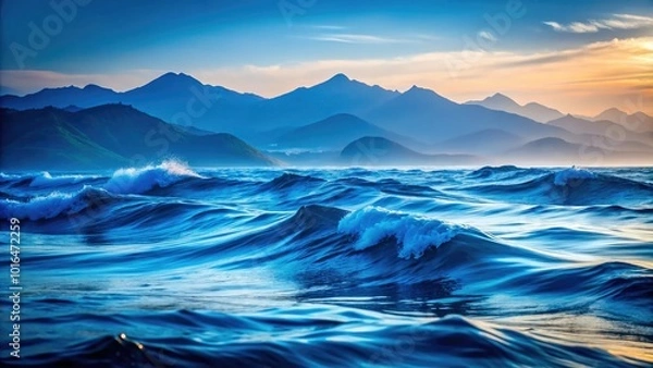 Fototapeta A serene backdrop featuring blue waves and soft mountain silhouettes, illustrating the tranquil beauty of an ocean water surface meeting rolling hills in harmony.
