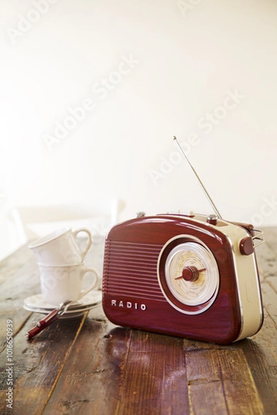 Obraz A vintage radio sits on a wooden table beside porcelain white mugs, bathed of morning light. It's time for tea. Vertical photo.