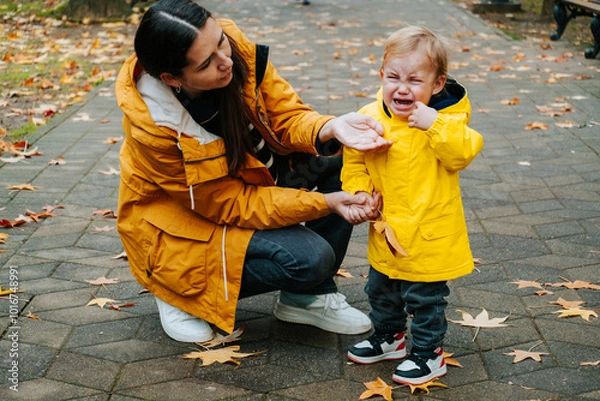 Fototapeta Young mother tries to calm her crying little son outdoor in the park. Raising  child concept.