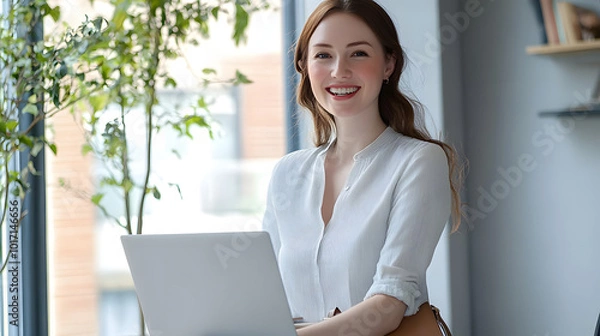 Fototapeta 綺麗なオフィスの窓辺でノートパソコンを持つ美しい女性　パソコンを抱え笑顔　左にコピースペースあり