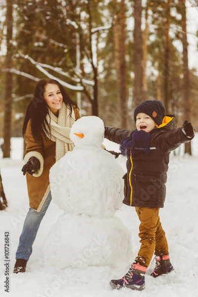 Obraz Happy family in warm clothing. Smiling mother and son making a snowman outdoor. The concept of winter activities