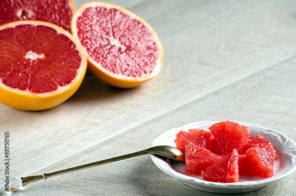 Obraz Slices of grapefruit on a plate, a spoon and a grapefruit