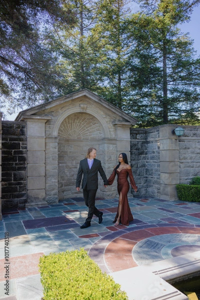 Fototapeta A stunning engagement photoshoot captures a beautifully diverse mixed couple walking hand in hand, completely surrounded by lush nature, joyfully celebrating their unique love story and commitment