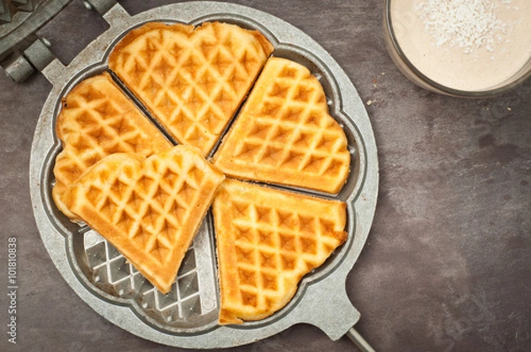 Fototapeta Home made heart shaped waffles served in a traditional cast iron waffle pan with a healthy peanut butter banana smoothie milkshake.