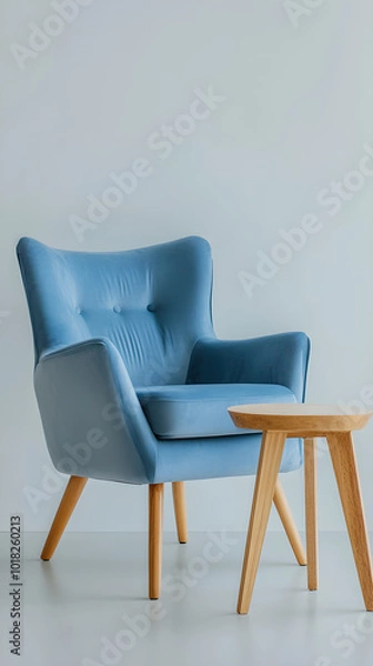 Fototapeta A soft blue armchair positioned next to a light wooden side table on a minimalist background brings a serene and inviting atmosphere