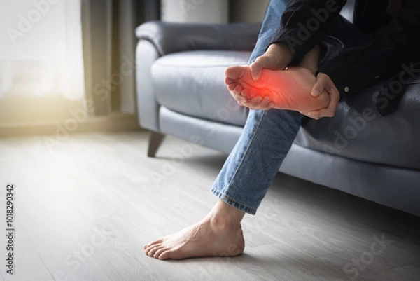 Obraz 발바닥 통증을 앓는 여성이 집 거실 소파에 앉아 아픈 발바닥을 주무르고있는 장면 