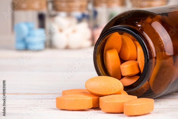 Obraz Orange pills in glass container with medicines in back