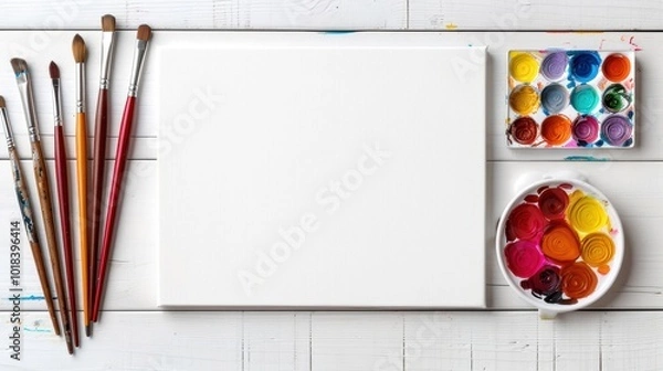 Fototapeta Art supplies neatly arranged with a blank canvas, watercolor palette, and brushes on a wooden table.