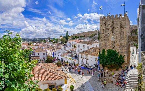 Fototapeta Obidos, Portugalia. Pejzaż miasta ze średniowiecznymi domami, murem i wieżą Albarra. Obidos to średniowieczne miasto, które wciąż znajduje się wewnątrz murów zamkowych i jest bardzo popularne wśród turystów.