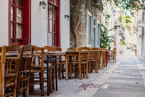 Obraz Quaint wooden tables set under blooming flowers create a welcoming ambiance along the narrow streets of Nafplio, showcasing the city's charming character.