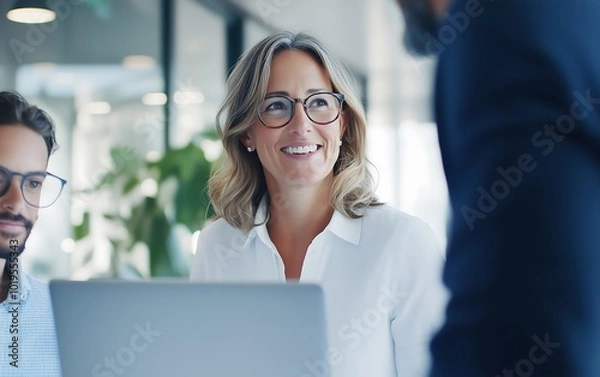 Fototapeta A woman smiles at colleagues in a modern office setting, showcasing collaboration and positivity in a professional environment.