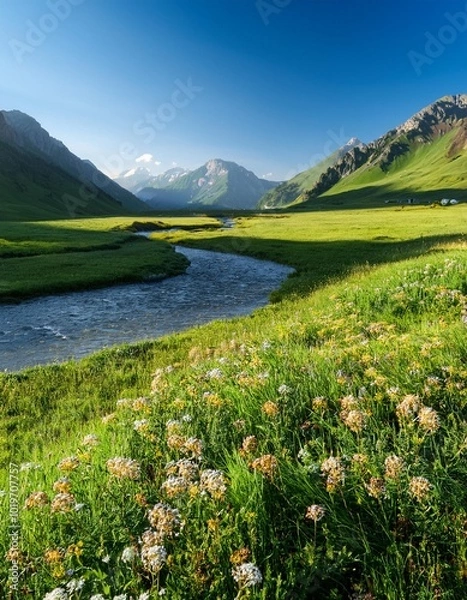 Fototapeta Lush Green Valley With a Slow-Moving River Winding Through Flower-Filled Meadows, Beneath Towering Mountains and Clear Blue Skies, in a Tranquil Morning Light
