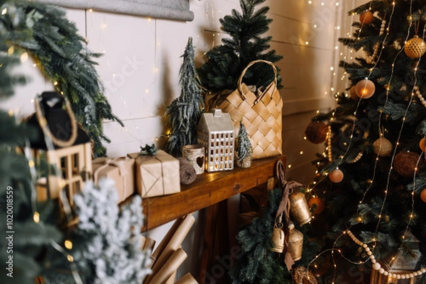 Fototapeta New Year's scene in a natural style: wooden decor, decorative houses. pine branches, wicker baskets and a carpet made of natural fibers. The Christmas tree shines with golden decorations and warm ligh
