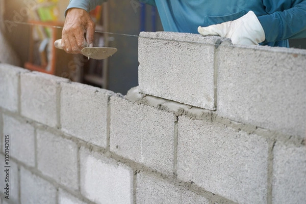 Obraz masonry worker make concrete wall by cement block and plaster at construction site