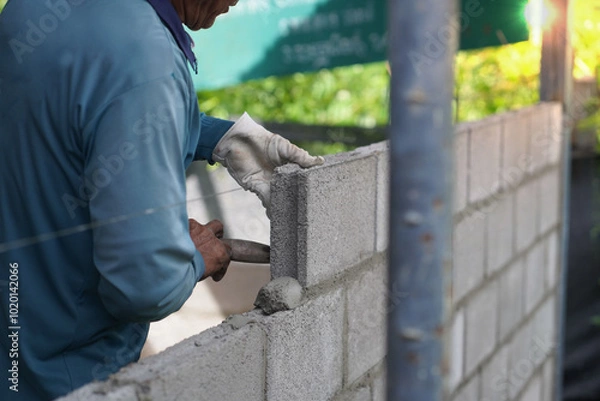 Obraz masonry worker make concrete wall by cement block and plaster at construction site