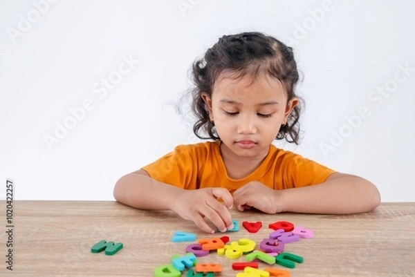 Fototapeta A cheerful little Asian girl enjoying playing with the wooden alphabet letters on the table