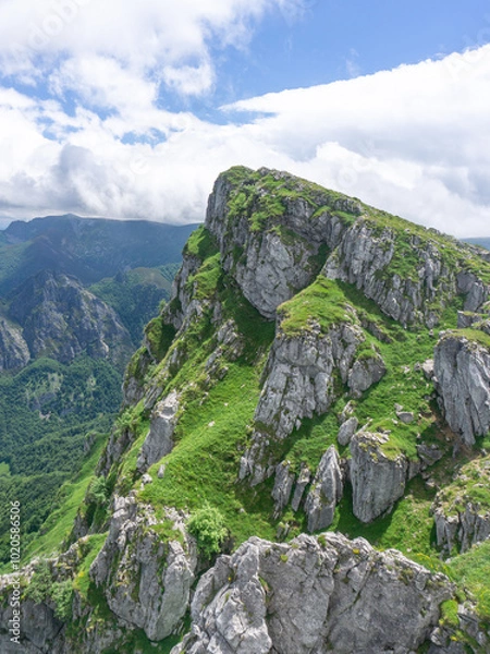 Fototapeta Mountain scenery with a dominant peak covered with green grass and limestone rock formations under a partly cloudy sky