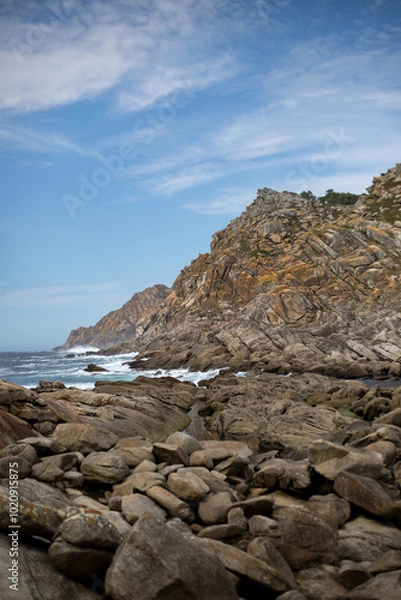 Fototapeta A rugged coastline with dramatic cliffs and crashing waves. The image showcases a rocky landscape, with large boulders scattered along the shore.