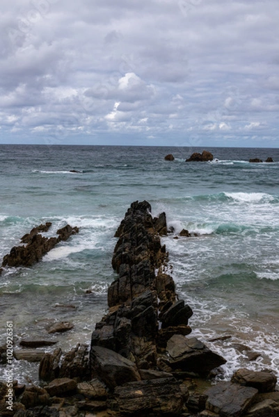 Obraz A dramatic seascape with crashing waves against a rocky breakwater, stretching towards the horizon. The stormy sky adds a sense of intensity to the scene.
