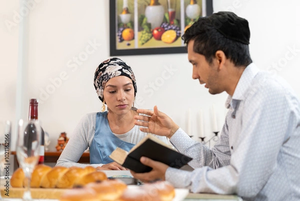 Obraz Jewish couple studying religious text together at home, traditional head coverings, Hanukkah meal setting, cultural traditions, spiritual discussion.