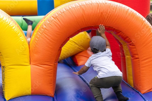 Fototapeta Boy in a baseball cap energetically climbs an inflatable structure at a colorful outdoor birthday party, enjoying the fun and active play