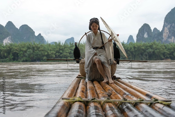 Obraz Hanfu girl holding an umbrella poses on bamboo raft on river with two cormorants. Xingping, China